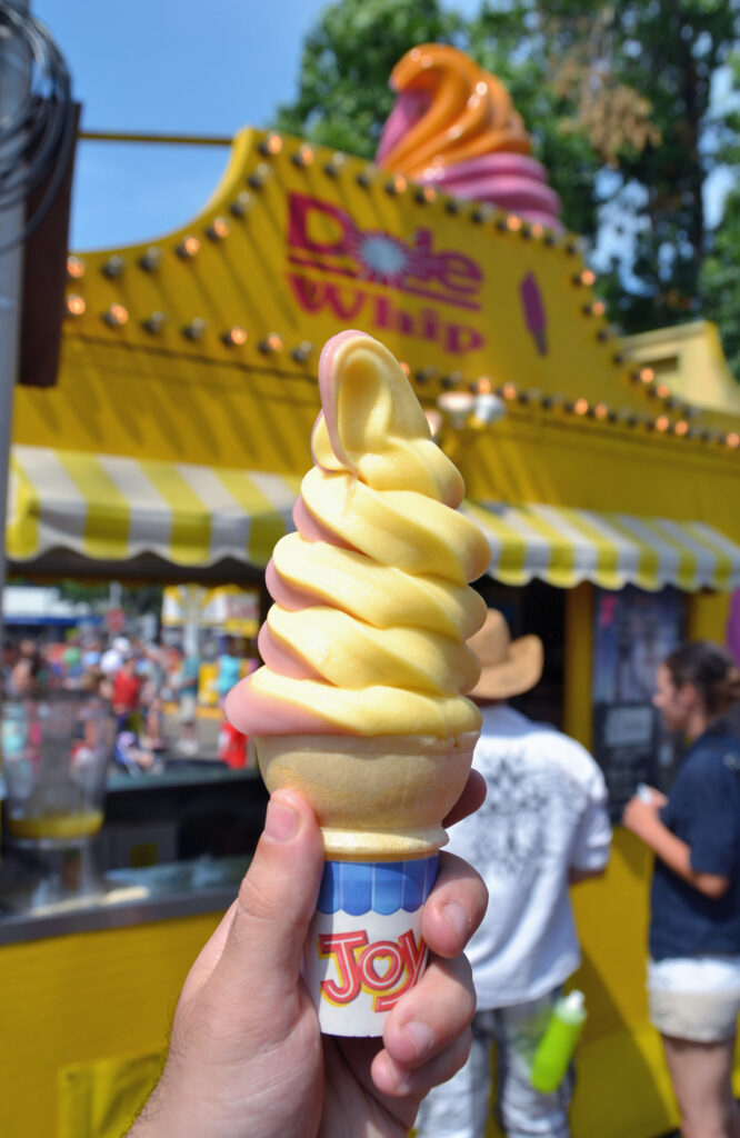 dole whip yellow and pink soft serve on cone in front of dole whip store